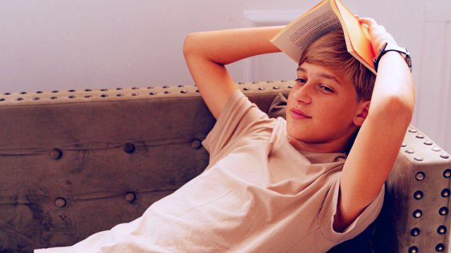boy on couch holding open book on head